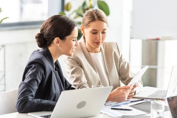 Due donne d'affari sorridenti in abiti formali a tavola in ufficio — Foto stock