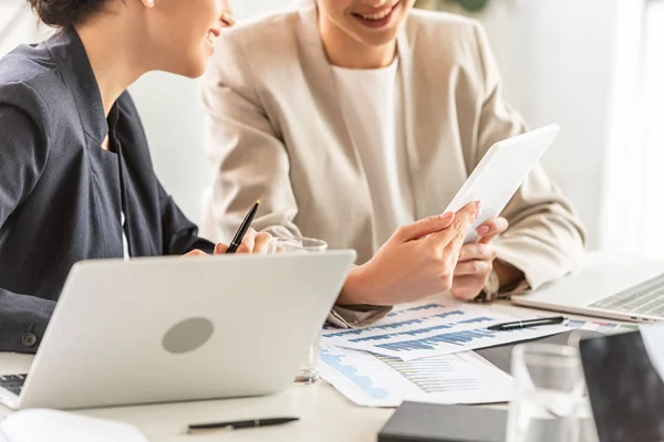 Частичный взгляд на двух деловых женщин в формальной одежде за столом с ноутбуками и цифровым планшетом в офисе — стоковое фото