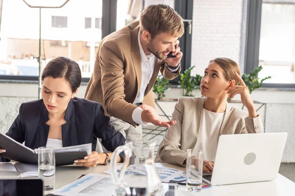 Businessman standing near colleagues in office and talking on smartphone — Stock Photo