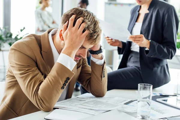 Partial view of businesswoman sitting on table near confused colleague and holding document — Stock Photo