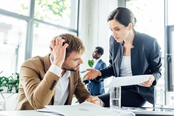 Businesswoman sitting on table near confused colleague and holding document — Stock Photo