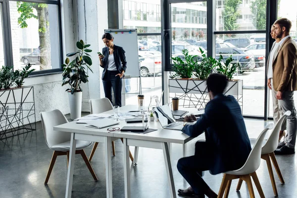 Vier multiethnische Kollegen, die im Büro digitale Geräte nutzen und arbeiten — Stockfoto