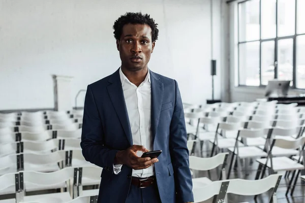 Hombre de negocios afroamericano en ropa formal celebración de teléfonos inteligentes en la sala de conferencias - foto de stock