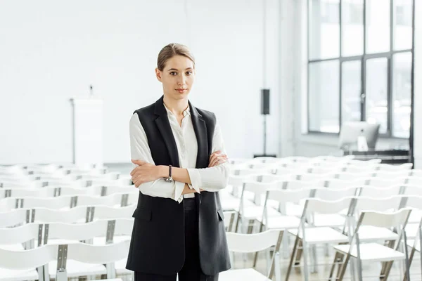 Attraente donna in abito formale con braccia incrociate in sala conferenze — Foto stock
