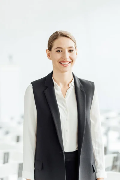 Atractiva y feliz mujer de negocios en ropa formal sonriendo en la sala de conferencias - foto de stock