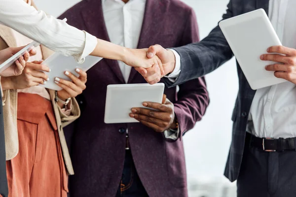 Cropped view of four multiethnic colleagues holding digital tablets and shaking hands — Stock Photo