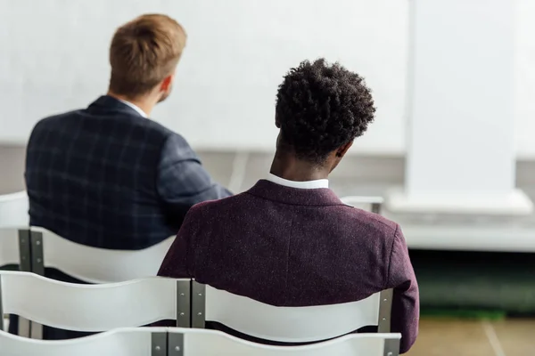 Back view of multiethnic businessmen sitting on chairs during conference — Stock Photo