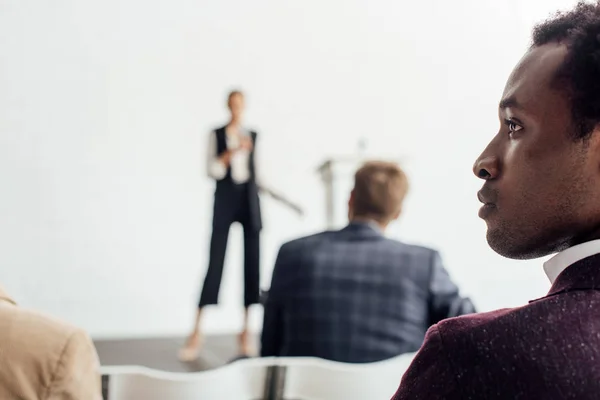 Selective focus of multiethnic businesspeople sitting during conference in conference hall — Stock Photo