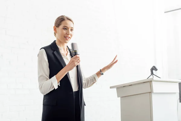 Séduisante femme d'affaires tenant microphone et parlant pendant la conférence dans la salle de conférence — Photo de stock