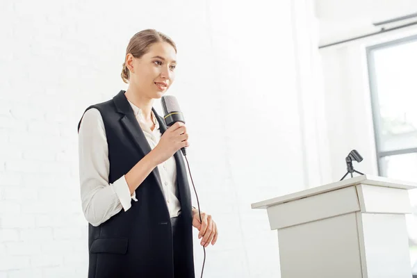 Attraktive Geschäftsfrau hält Mikrofon in der Hand und spricht während der Konferenz im Konferenzsaal — Stockfoto