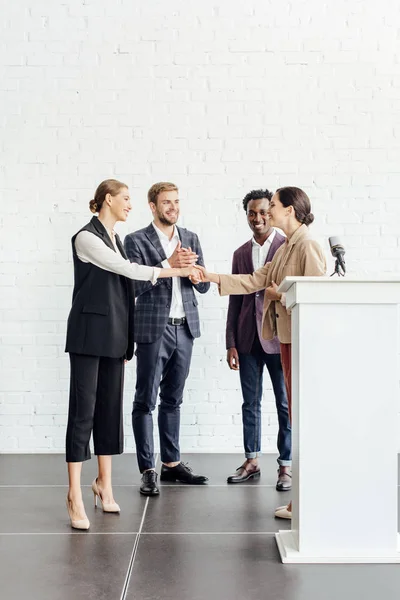 Cuatro colegas multiétnicos en ropa formal hablando y dándose la mano - foto de stock