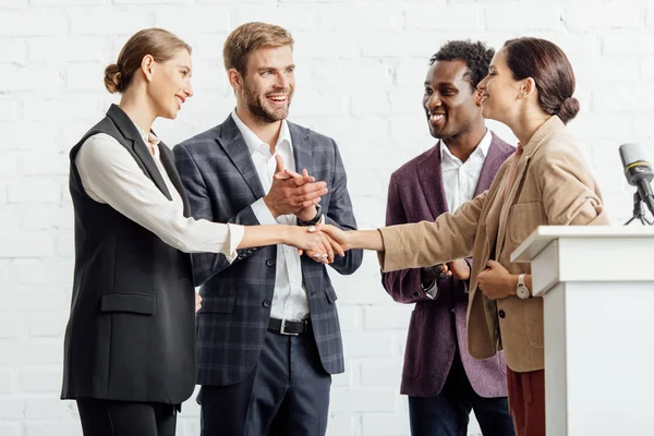 Cuatro colegas multiétnicos en ropa formal hablando y dándose la mano - foto de stock