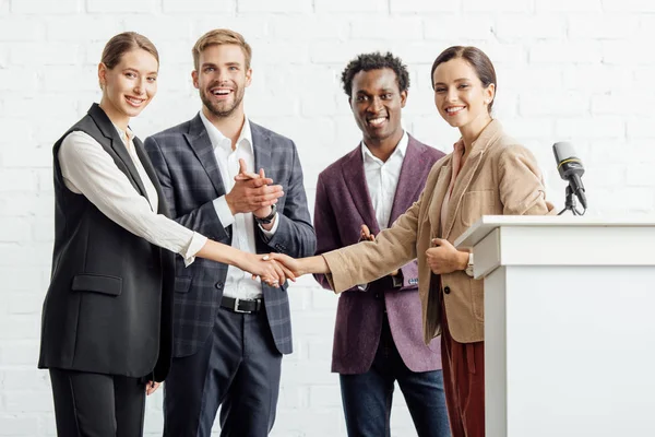 Four multiethnic colleagues in formal wear talking and shaking hands in conference hall — Stock Photo