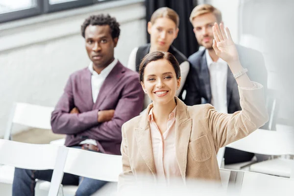 Selective focus of attractive woman in formal wear raising hand during conference — Stock Photo