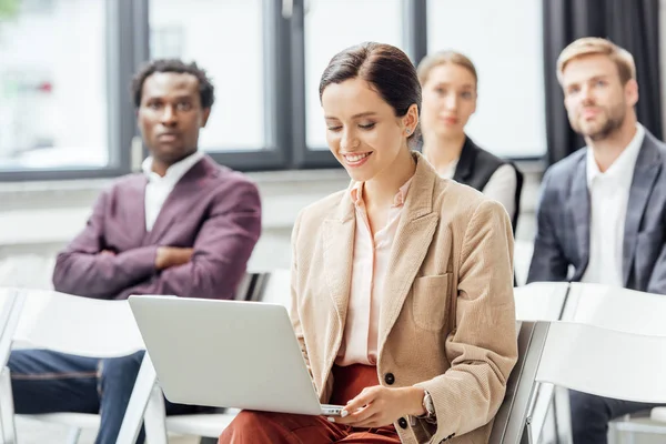 Selective focus of attractive woman in formal wear holding laptop during conference — Stock Photo