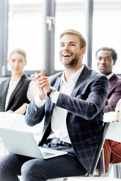 Selective focus of businessman in formal wear holding laptop and clapping during conference — Stock Photo