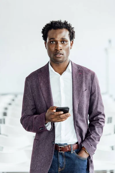 Hombre de negocios afroamericano en ropa formal celebración de teléfonos inteligentes en la sala de conferencias - foto de stock