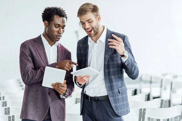 Two multiethnic colleagues in formal wear using digital tablets in conference hall — Stock Photo