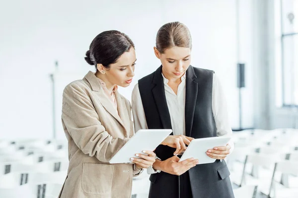 Dos colegas atractivos en ropa formal usando tabletas digitales en la sala de conferencias - foto de stock