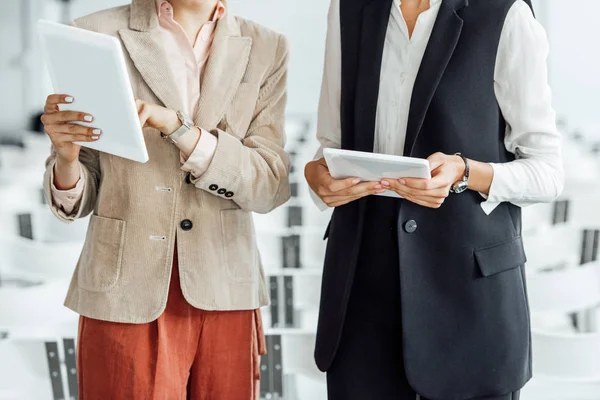 Vue recadrée de deux collègues en tenue de cérémonie utilisant des tablettes numériques dans la salle de conférence — Photo de stock