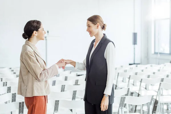 Two attractive colleagues in formal wear shaking hands in conference hall — Stock Photo