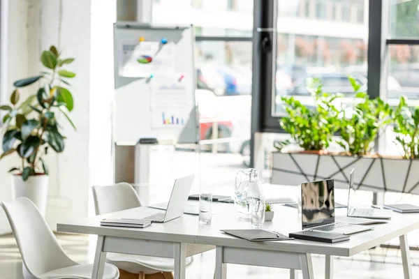 Oficina con mesa, sillas, plantas verdes y dispositivos digitales - foto de stock