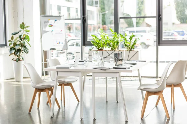 Interior de la oficina con mesa, sillas, plantas verdes y dispositivos digitales - foto de stock