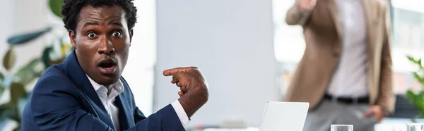 Панорамный снимок шокированного африканского бизнесмена, указывающего пальцем на себя в офисе — стоковое фото