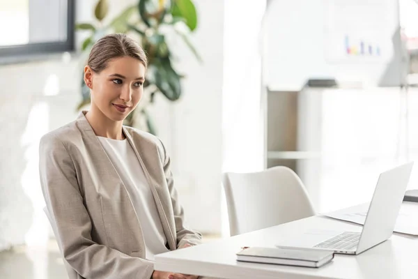 Attrayant femme d'affaires en tenue formelle regardant ordinateur portable au bureau — Photo de stock