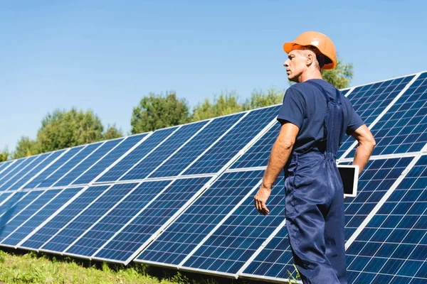 Back view of handsome engineer in overalls and hardhat holding digital tablet — Stock Photo