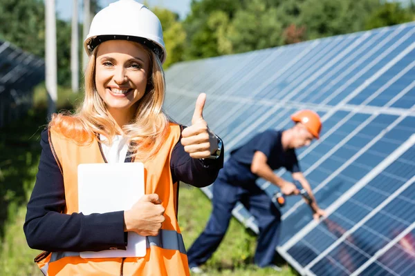 Atractiva mujer de negocios en hardhat mostrando el pulgar hacia arriba y sosteniendo la tableta digital - foto de stock