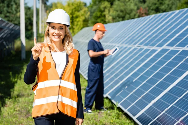 Atractiva mujer de negocios en hardhat sonriendo y mostrando gesto de idea - foto de stock