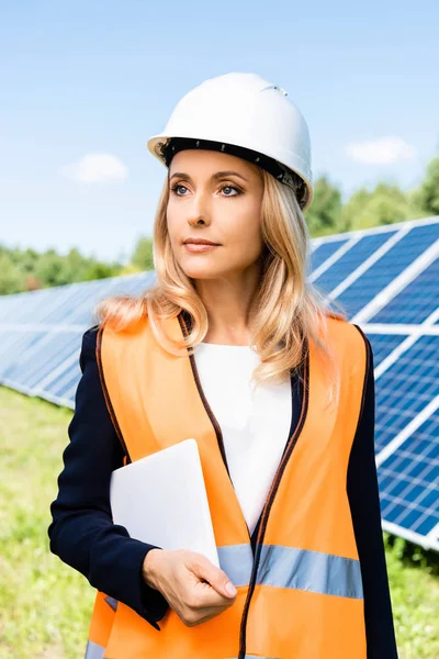 Attractive businesswoman in hardhat holding digital tablet and looking away — Stock Photo