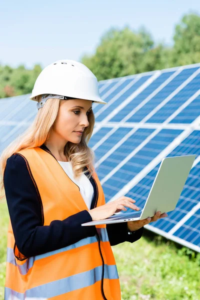 Attractive businesswoman in hardhat and safety vest using laptop — Stock Photo