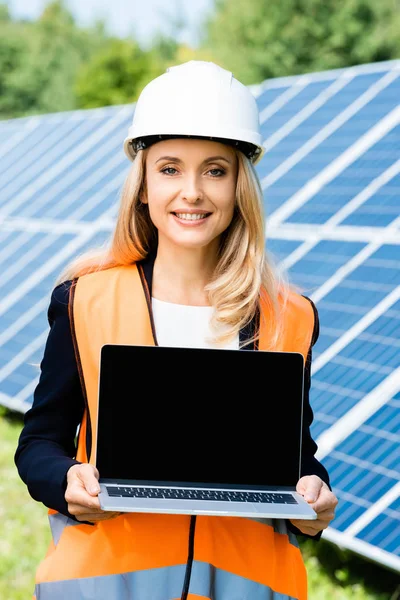 Attractive businesswoman in hardhat and safety vest holding laptop with copy space — Stock Photo