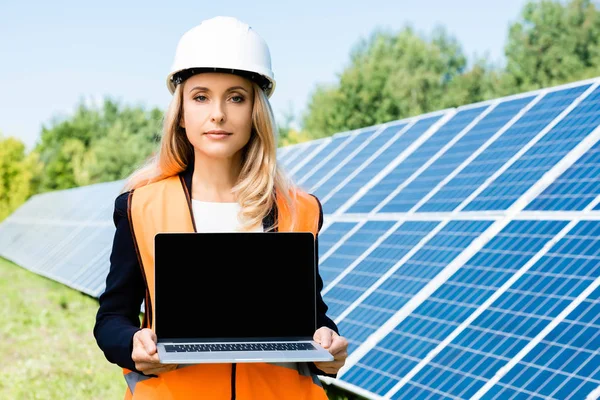 Attractive businesswoman in hardhat and safety vest holding laptop with copy space — Stock Photo