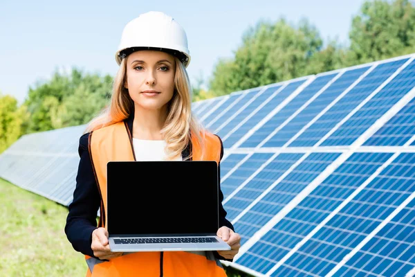 Atractiva mujer de negocios en hardhat y chaleco de seguridad que sostiene el ordenador portátil con espacio para copias - foto de stock