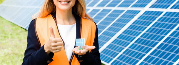 Panoramic shot of businesswoman in safety vest holding solar battery model — Stock Photo