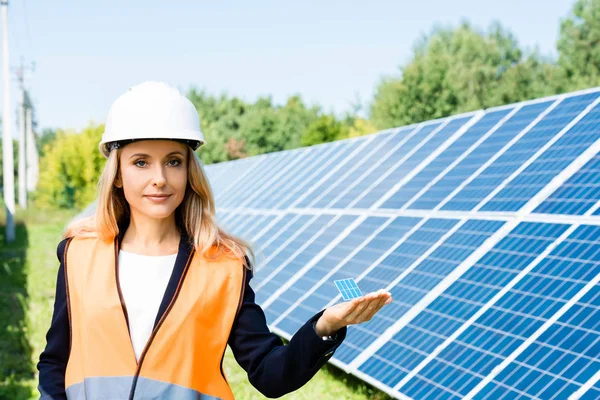 Atractiva mujer de negocios en chaleco de seguridad celebración de modelo de batería solar - foto de stock