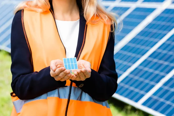 Cropped view of businesswoman in safety vest holding solar battery model — Stock Photo