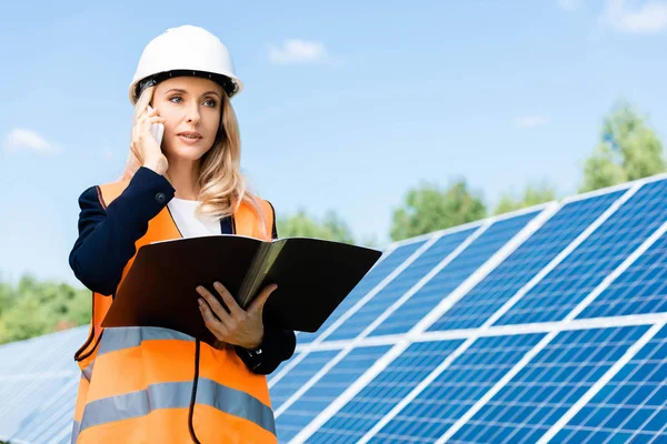 Businesswoman in safety vest holding folder and talking on smartphone — Stock Photo