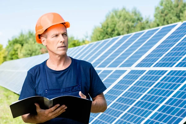 Handsome engineer in t-shirt and orange hardhat holding folder — Stock Photo