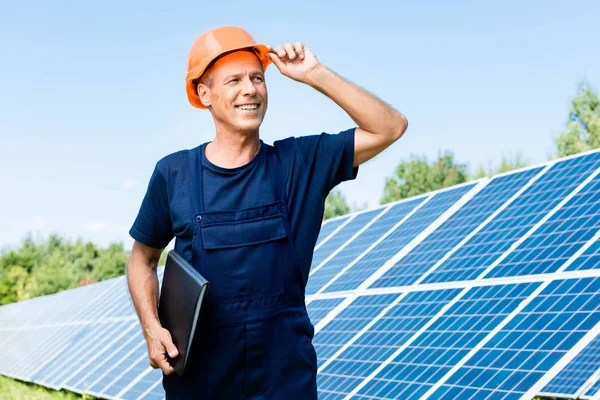 Schöner Ingenieur in T-Shirt und orangefarbenem Hut, lächelnd und mit Ordner in der Hand — Stockfoto