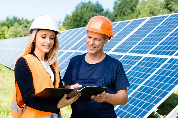 Ingeniero guapo y atractiva mujer de negocios hablando y sosteniendo carpeta - foto de stock