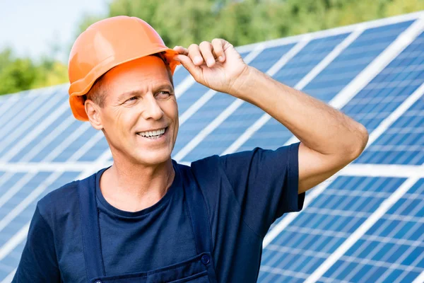 Handsome engineer in t-shirt and orange hardhat smiling and looking away — Stock Photo