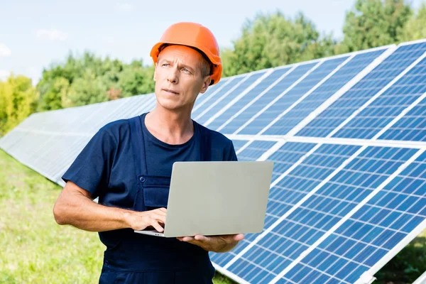 Schöner Ingenieur in T-Shirt und orangefarbenem Bollenhut mit Laptop — Stockfoto