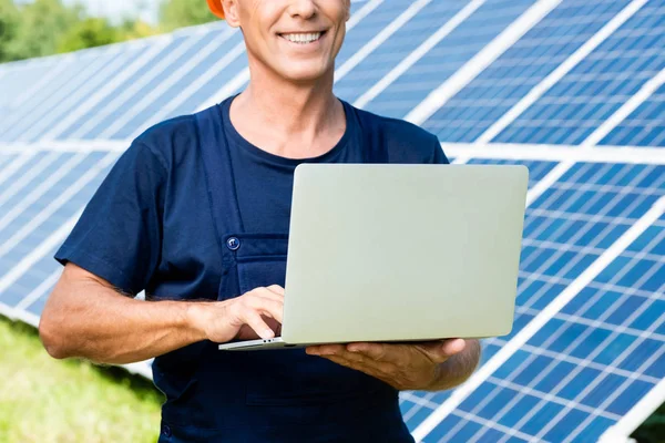 Vue recadrée de l'ingénieur en t-shirt souriant et tenant ordinateur portable — Photo de stock