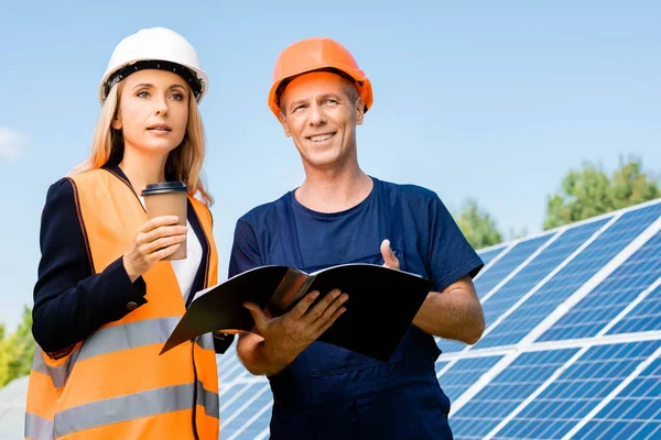 Ingeniero guapo y mujer de negocios sonriendo y sosteniendo carpeta - foto de stock