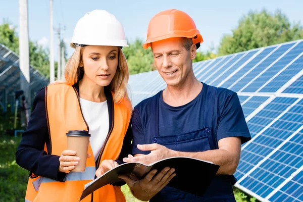 Ingeniero guapo y mujer de negocios hablando y sosteniendo carpeta - foto de stock