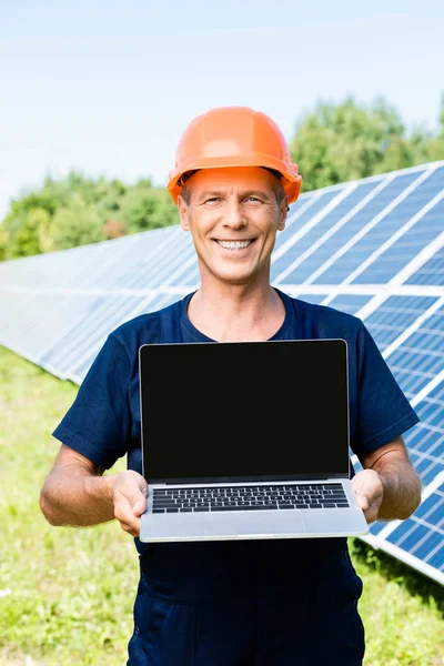Engenheiro bonito em t-shirt e hardhat laranja sorrindo e segurando laptop com espaço de cópia — Fotografia de Stock